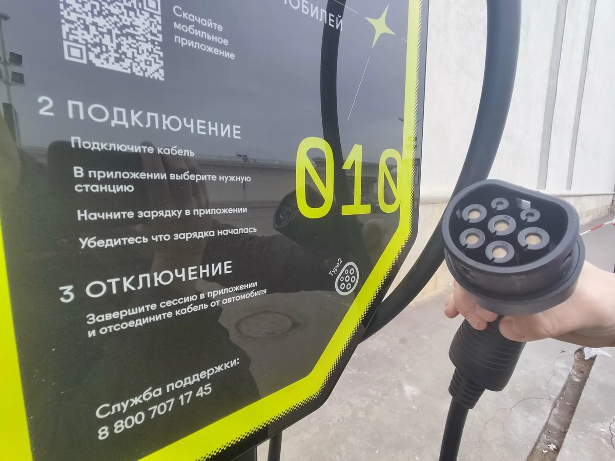 Коннектор зарядной станции в руке водителя, инструкция на станции